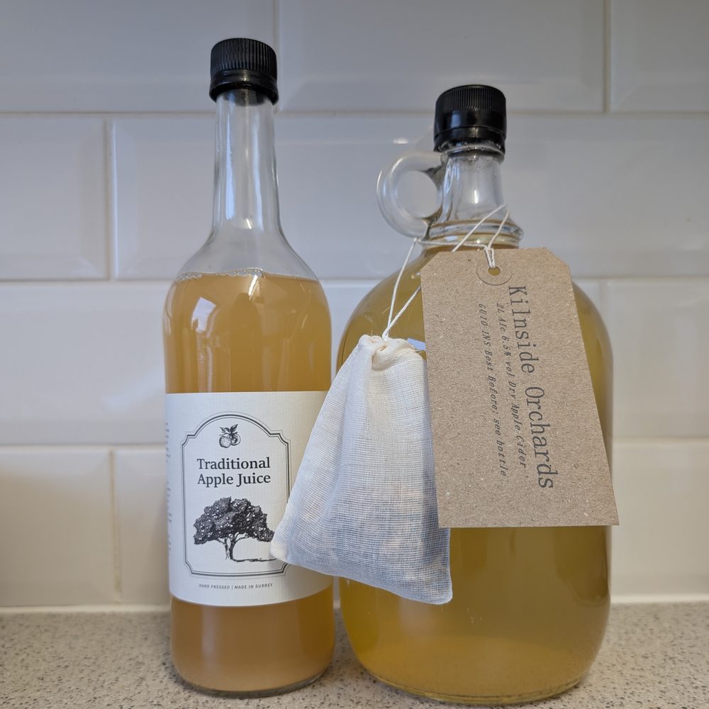 A bottle of apple juice and a flagon of dry cider with a spice bag for mulling