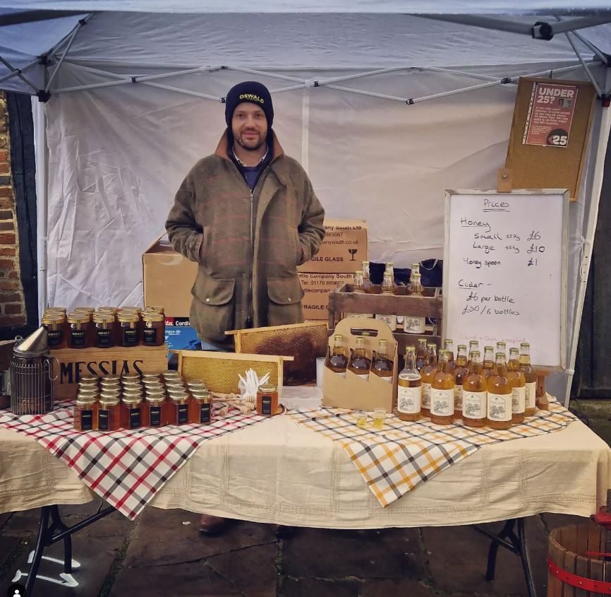 Honey, cider, frames of honeycomb and a bee smoker laid out on a table
