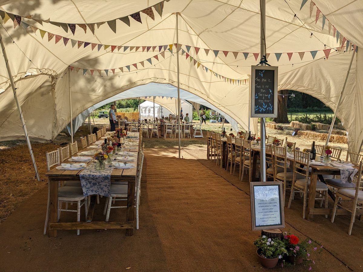 Long wooden tables with floral runners and wildflowers under a marquee strung with bunting