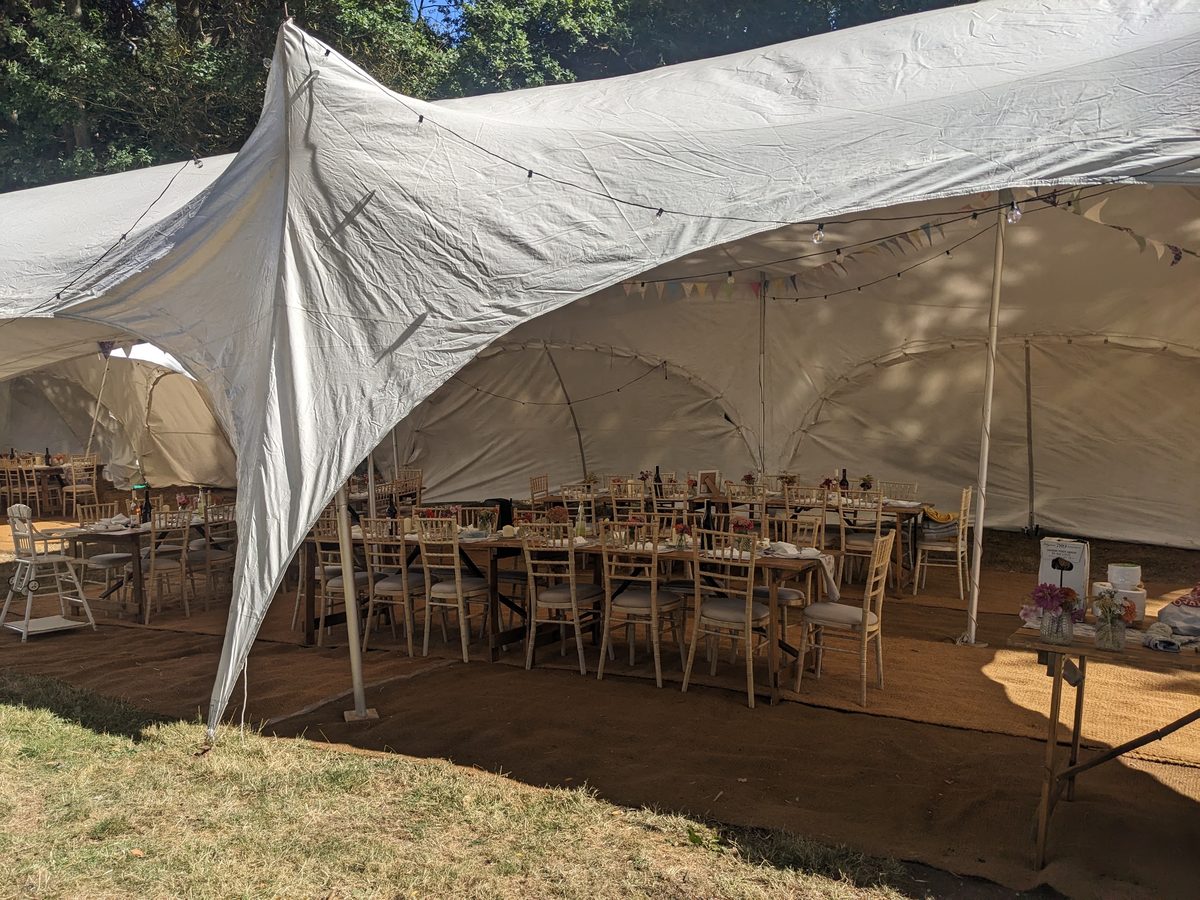 The marquee from outside, its canvas peaks under the trees, tables laid within